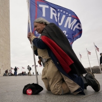 A man dressed as George Washington is praying while holding a Trump 2020 flag