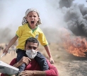 A distressed child rides atop the shoulders of a man, surrounded by fire and destruction. Public domain image by Pixabay user Hosny Salah.